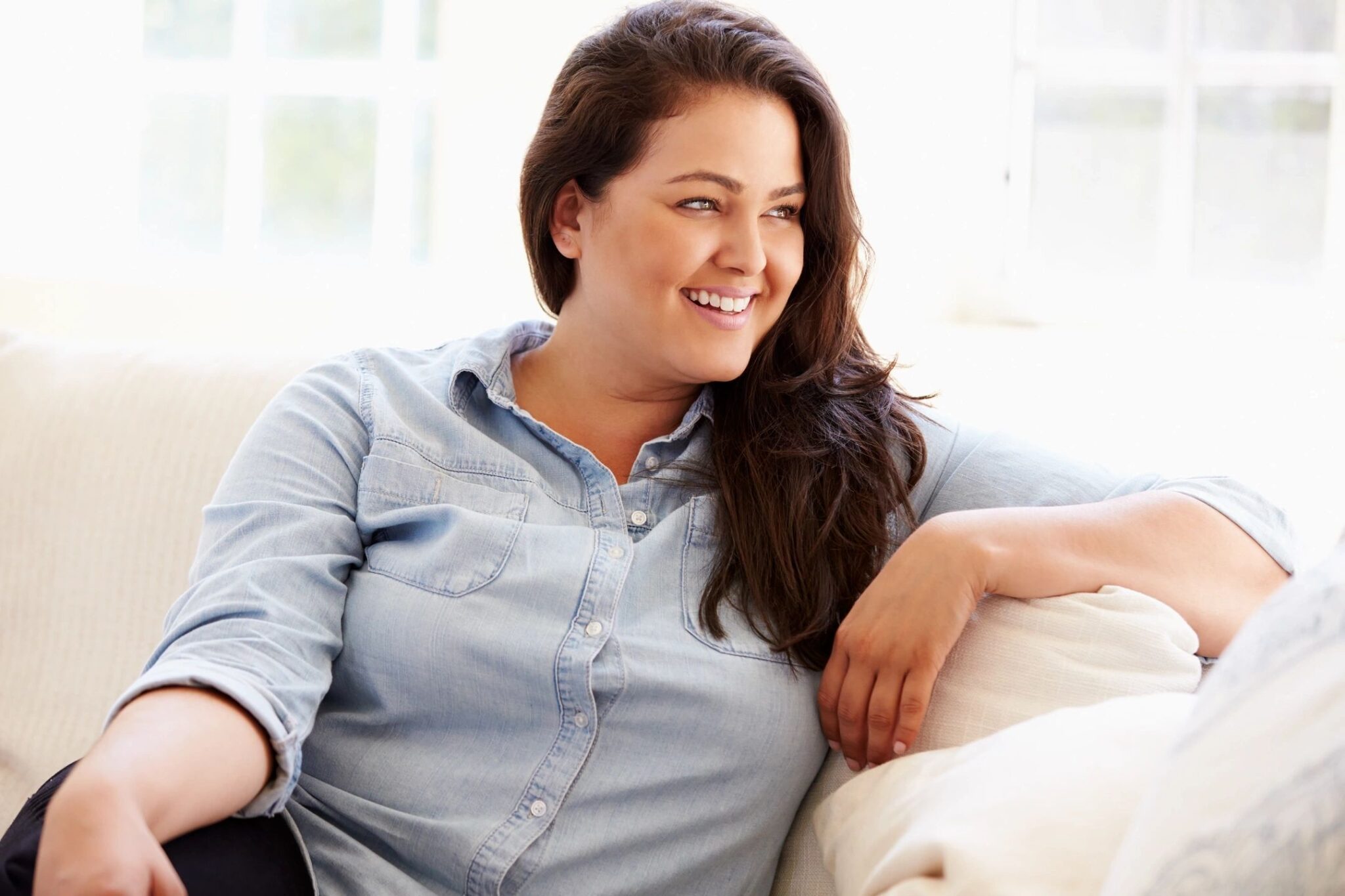 A woman sitting on top of a couch next to a window.