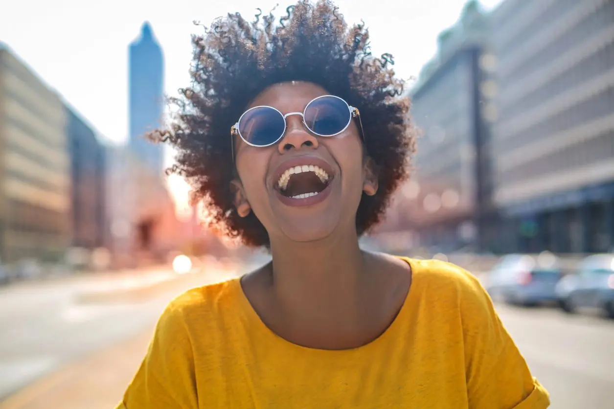 A woman with sunglasses and a yellow shirt is laughing.