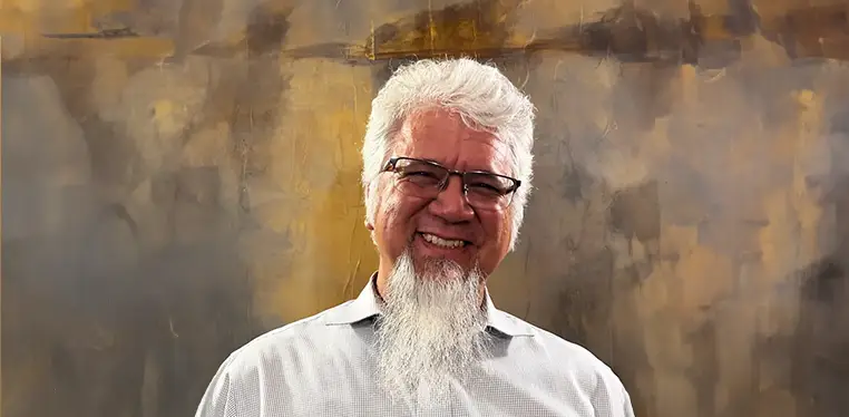 A man with white hair and glasses smiling.