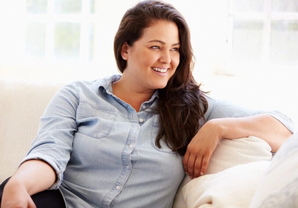 A woman sitting on top of a couch next to a window.